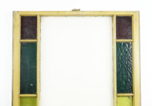 Antique pine framed stained glass window with a tall central opening and narrow colored panes at the sides in purple, green, and clear tones, shown front on with wear visible on the frame.