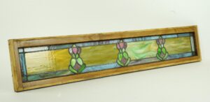 Art Nouveau stained glass window in a light wood pine frame, shown at an angle with a long rectangular design and three floral leaded motifs in multicolored panes.