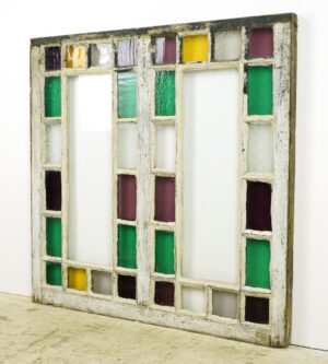 Antique Queen Anne stained glass window with a weathered pine frame and intact multicolor panes in a grid layout.