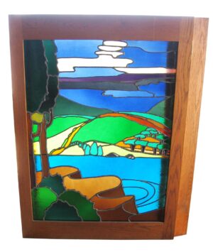 Backlit stained glass window in a wooden frame, showing a pastoral landscape with hills, water, trees, and clouds in multiple colors.