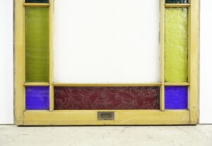 Antique pine framed Queen Anne stained glass window with clear center glass, green side panes, purple lower corners, and a red lower panel, shown in the frame with visible wear.