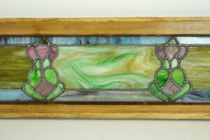 Art Nouveau stained glass window with a pine frame and symmetrical leaded floral motif in multicolor glass panels.