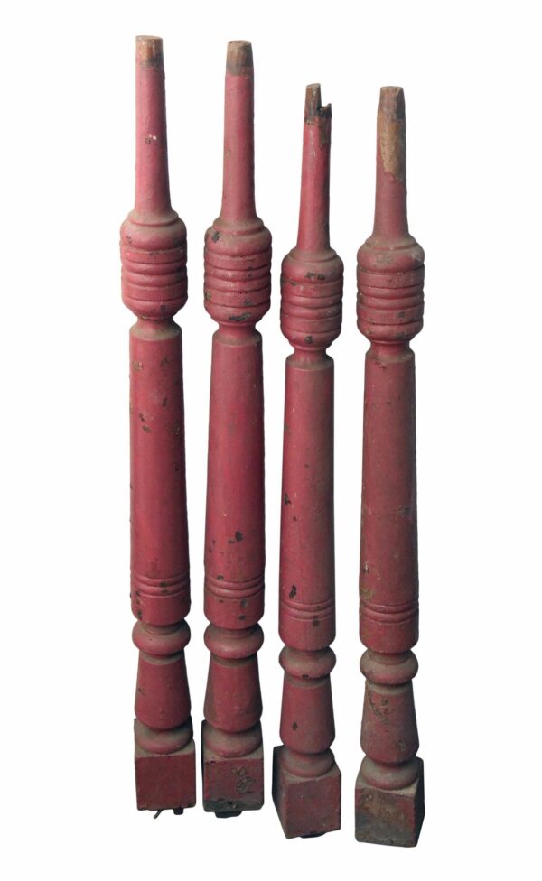 Set of four red wooden stair spindles with carved turned details and visible wear, shown upright in a front-facing view.