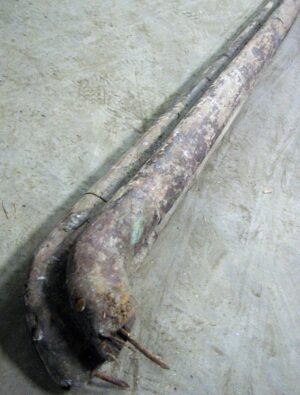 Close-up of a reclaimed wooden handrail showing the curved end and worn medium wood tone surface, with visible spindle slots.