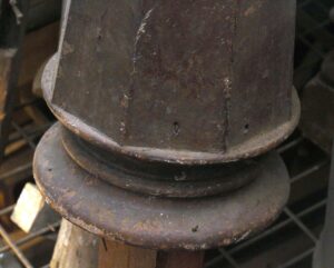 Close-up of a dark wood tone wooden newel post with a rounded base and carved upper section, shown in a worn, restorable condition.