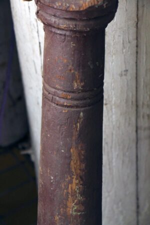 Close-up of a brown wooden staircase newel post with carved ring details and visible wear.