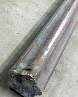 Close-up of a reclaimed wooden banister handrail with a dark wood tone, shown at an angle with one end visible.