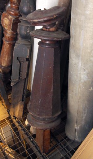 Dark wood tone wooden newel post with a carved top and tapered body, shown close up.