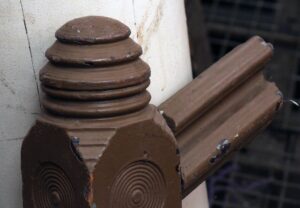 Close-up of a traditional carved wooden staircase newel post with bull's-eye detailing and a brown finish, shown at an angle.