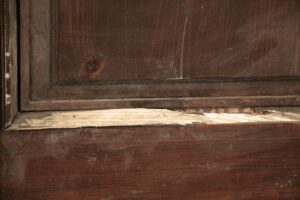 Close-up of a dark wood tone wooden door panel with visible wear and a missing panel section.
