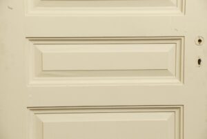 Close-up of a white wooden door with three recessed panels and visible lock holes on the right edge.