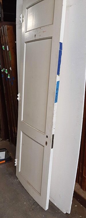 White wooden passage door with three panels, shown at an angle with some original hardware still attached and visible wear on the surface.