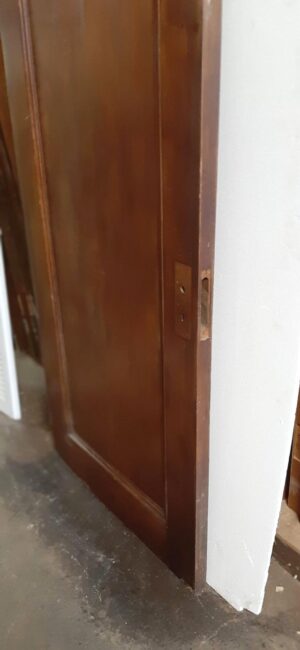 Walnut passage door shown at an angle with the latch edge and one paneled side visible, in a dark wood tone.