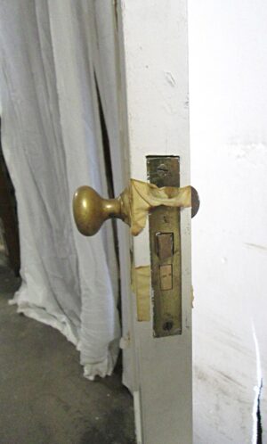 Close-up of a white wood passage door with one vertical panel, showing the brass knob and latch edge in a right-swing orientation.