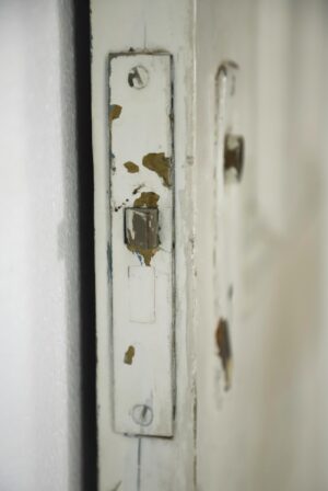 Close-up of the white painted passage door edge with a worn latch plate and chipped paint showing surface wear.