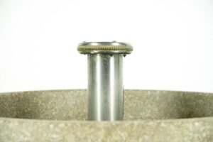 Close-up of a gray metal hand wash fountain showing the central foot-control assembly and the worn rim of the basin.