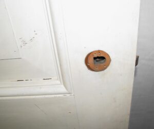 Close-up of a white two-panel wood passage door with a missing round hardware plate and visible wear around the latch opening.