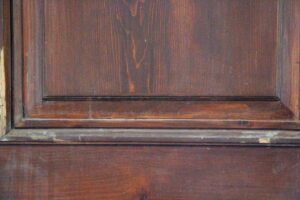 Close-up of a dark wood tone wooden door panel with visible frame edges and one recessed section.
