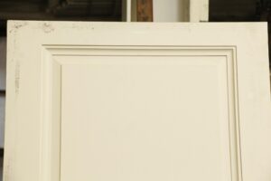 White wooden door with three raised panels, shown in a close-up of the upper section and frame edge.