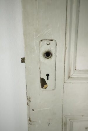 Close-up of a white painted five-panel door edge with an old lock plate and visible surface wear and chipped paint.