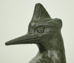 Close-up of a black bronze woodpecker statue showing the head and beak in profile.