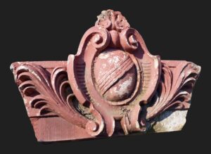 Decorative terra cotta keystone with an ornate carved scroll design and a central oval medallion, shown in close-up.