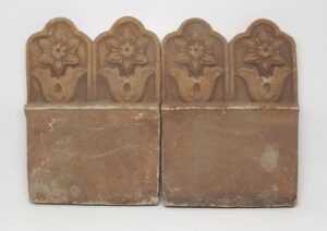 Pair of terra cotta pieces with floral relief tops, shown side by side as a set.