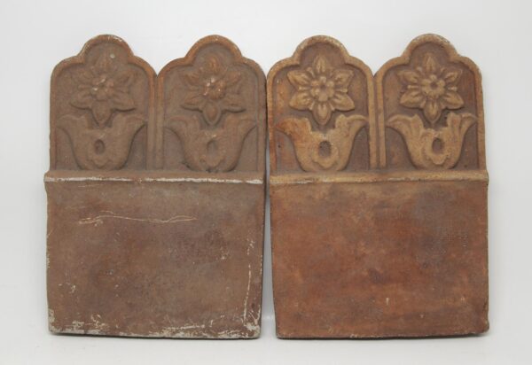 Pair of terra cotta pieces with a floral relief top and flat lower section, shown side by side as a set.