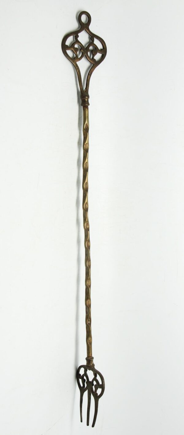 Single brass fireplace fork with a cutout handle and bottom, shown vertically with a twisted shaft and antique brass finish.