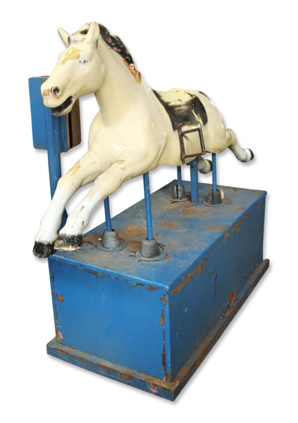 Vintage horse arcade ride with a white horse figure on a blue base, shown in three-quarter view with worn enamel and visible metal support poles.