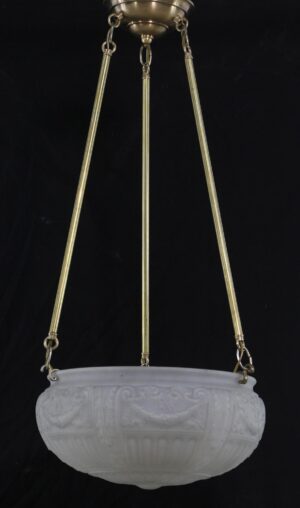 White cast glass dish pendant light suspended from three antique brass poles with a brass canopy and ornate relief detail on the bowl.