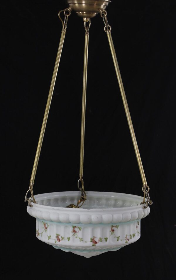 White cast glass pendant light with painted pink floral and green foliate details, suspended from three antique brass poles and shown with the brass canopy above.