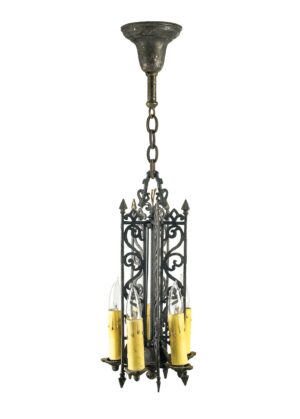 Spanish-style pendant light with black painted brass, ornate scrollwork, and five exposed candle-style bulbs hanging from a chain.