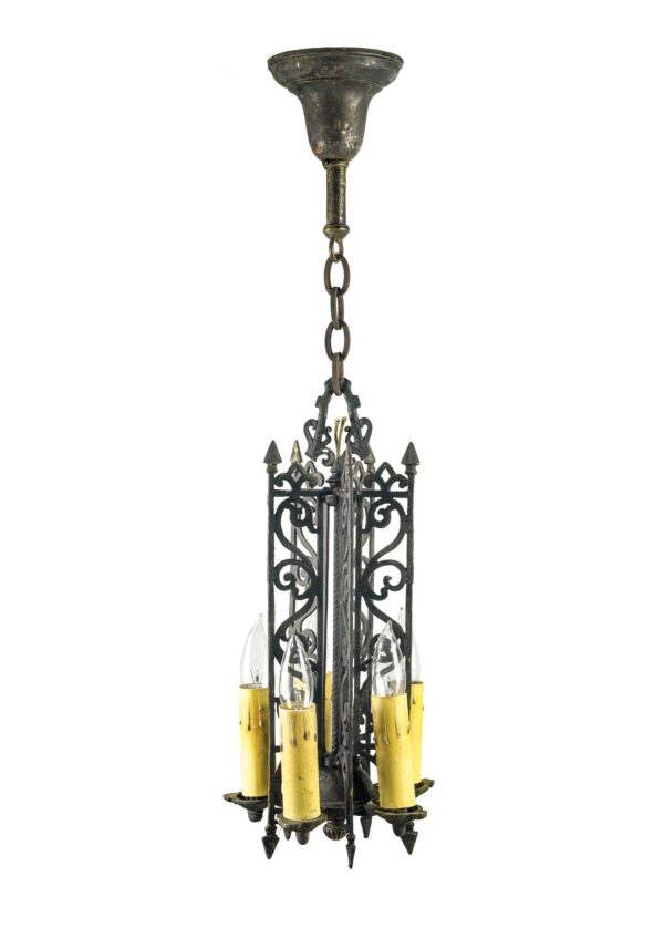 Spanish-style pendant light with black painted brass, ornate scrollwork, and five exposed candle-style bulbs hanging from a chain.