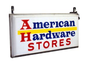 Vintage hanging American Hardware Stores sign with blue, red, white, and yellow lettering, shown at an angle with two mounting brackets visible on top.