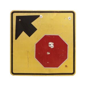 Vintage yellow metal road sign with a black left-pointing arrow and a red stop symbol, showing visible wear and peeling paint.