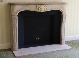 Louis XV limestone mantel with carved detailing and a replacement hearth, shown installed in a room.