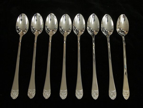 Eight silver iced teaspoons with long handles and Art Deco patterned ends arranged in a row.