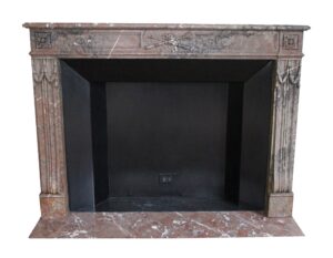 Front view of a carved marble mantel with fluted legs, flower motifs, crossed tools in the apron, and a dark firebox opening.