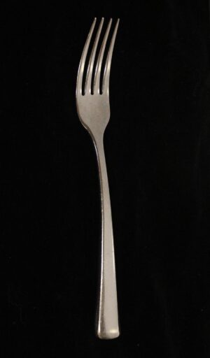 A stainless steel dinner fork with a long handle and four tines shown upright on a dark background.