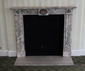 A marble mantel with gray veining and figural cameos, shown with the opening centered and the hearth stone below.