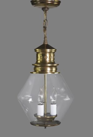 Hanging lantern light with an antique brass body and clear glass shade, shown with three candlestick sockets visible inside.