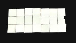 Set of 21 plain square white ceramic wall tiles shown in a grid, with a shiny surface and visible age-related chips and scrapes on several pieces.