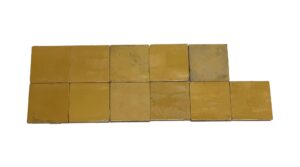 Set of 12 square yellow ceramic wall tiles with a shiny crackled surface and visible age-related chips and scrapes, shown arranged in two staggered rows.