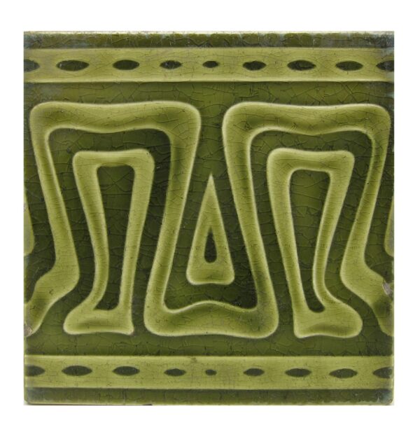 Close-up of a green ceramic geometric tile with raised symmetrical patterns and dotted border bands.