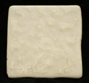 Off white ceramic wall tile with a textured surface and rounded corners, shown close up with minor age-related imperfections and chips.