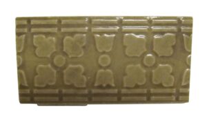 Tan ceramic decorative tile with a raised floral and geometric pattern shown in a close-up view.