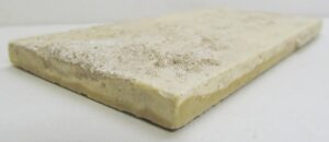 Close-up of a tan ceramic geometric tile with visible age-related imperfections and minor chips along the edges.