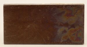 Brown ceramic tile with visible age-related scratches and minor wear across the surface.