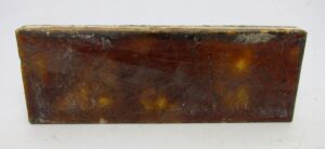 Burnt brown ceramic tile with visible age-related chips and scrapes.